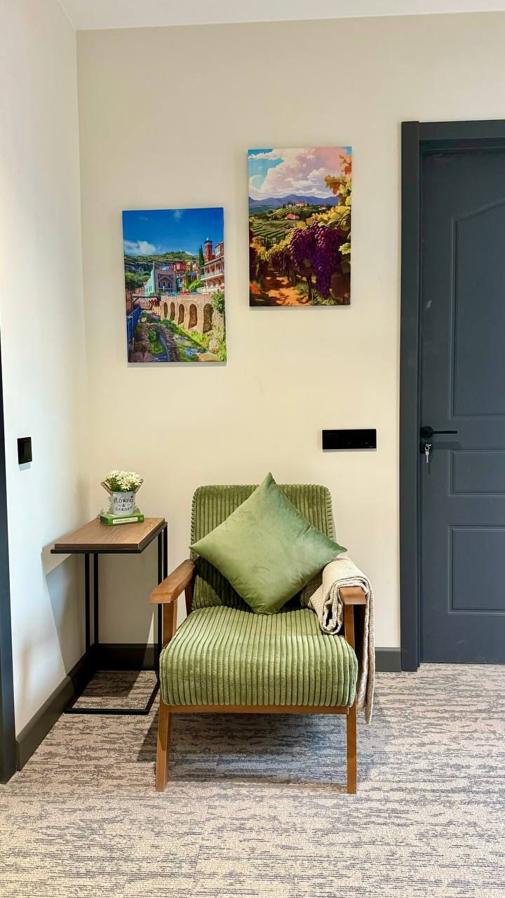 Un pasillo con una butaca tapizada de verde, una mesita con un jarrón de flores y dos cuadros en la pared.