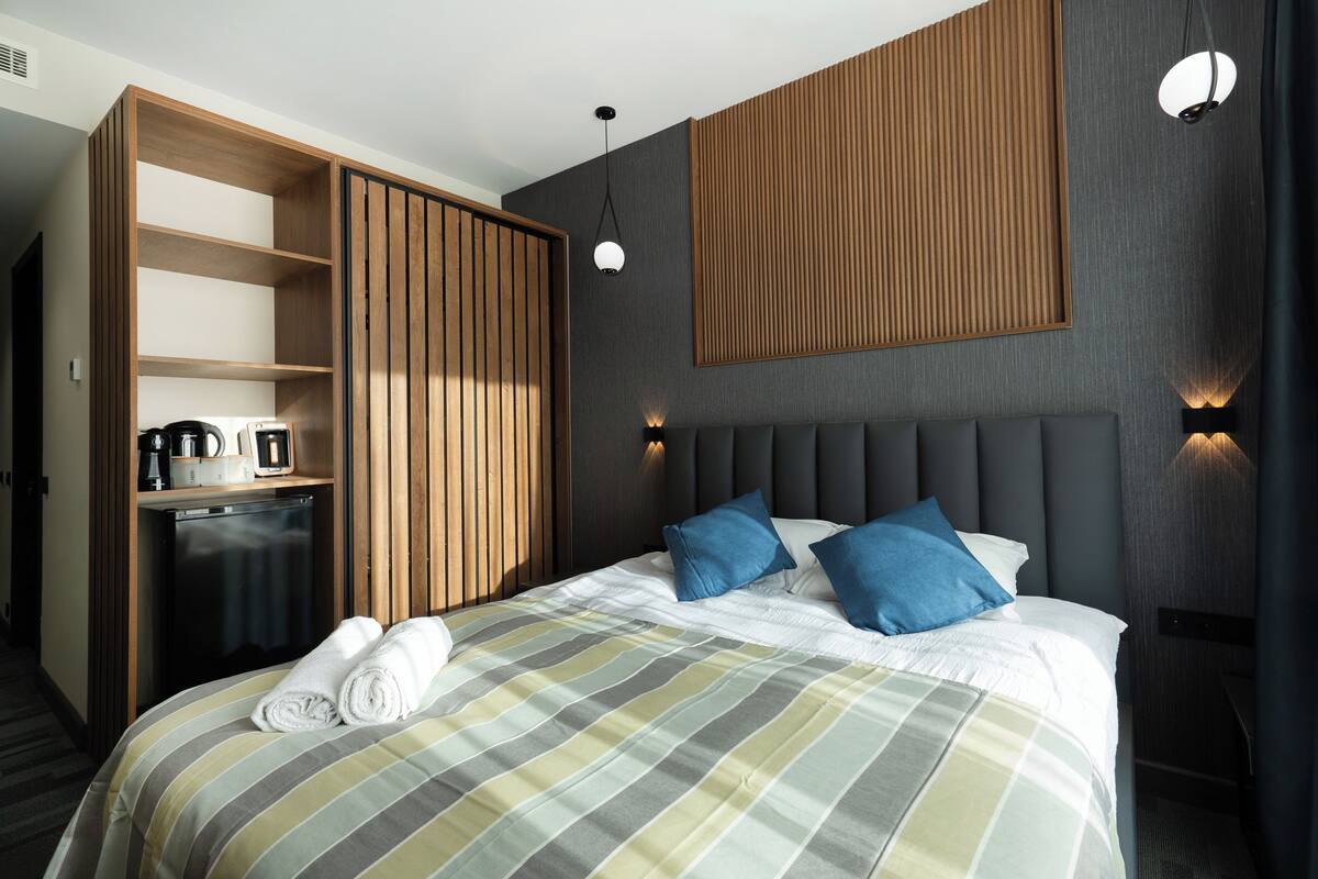 Une chambre d’hôtel comprenant un lit, une armoire en bois, une petite kitchenette et un panneau fixé au mur.
