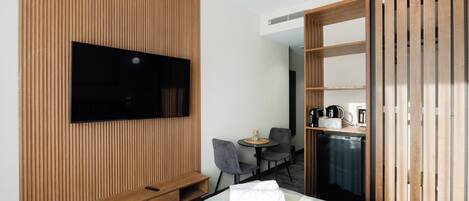 Une chambre d’hôtel moderne dotée d’un grand lit, d’un téléviseur à écran plat fixé sur un mur en panneaux de bois, d’une petite table ronde avec deux chaises et d’une armoire aux portes coulissantes.