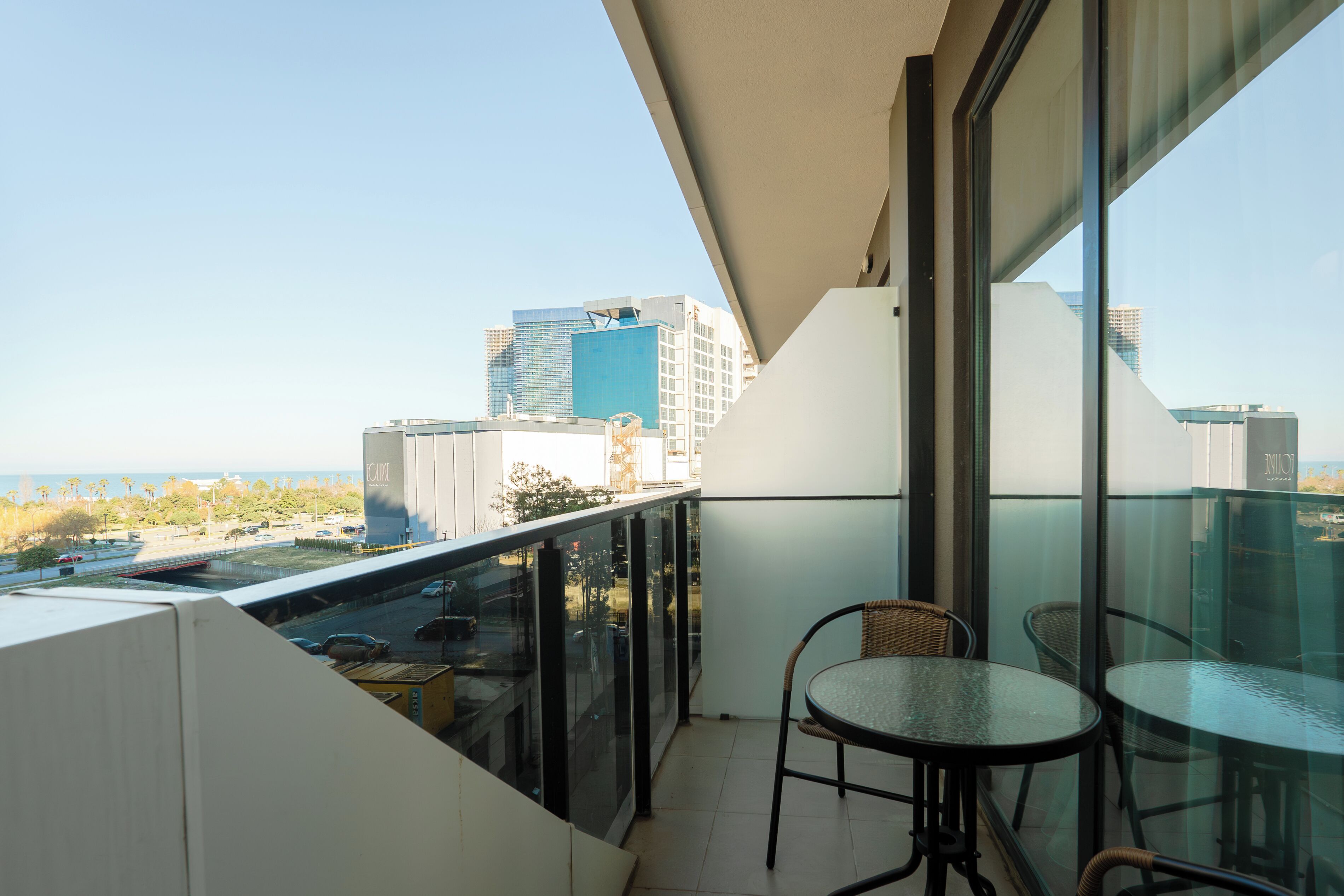 A balcony with a glass railing, two wicker chairs, and a table.