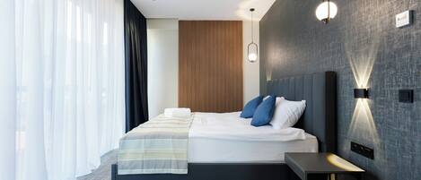 A modern hotel room with a large bed, a bedside table, and a wall-mounted light fixture.