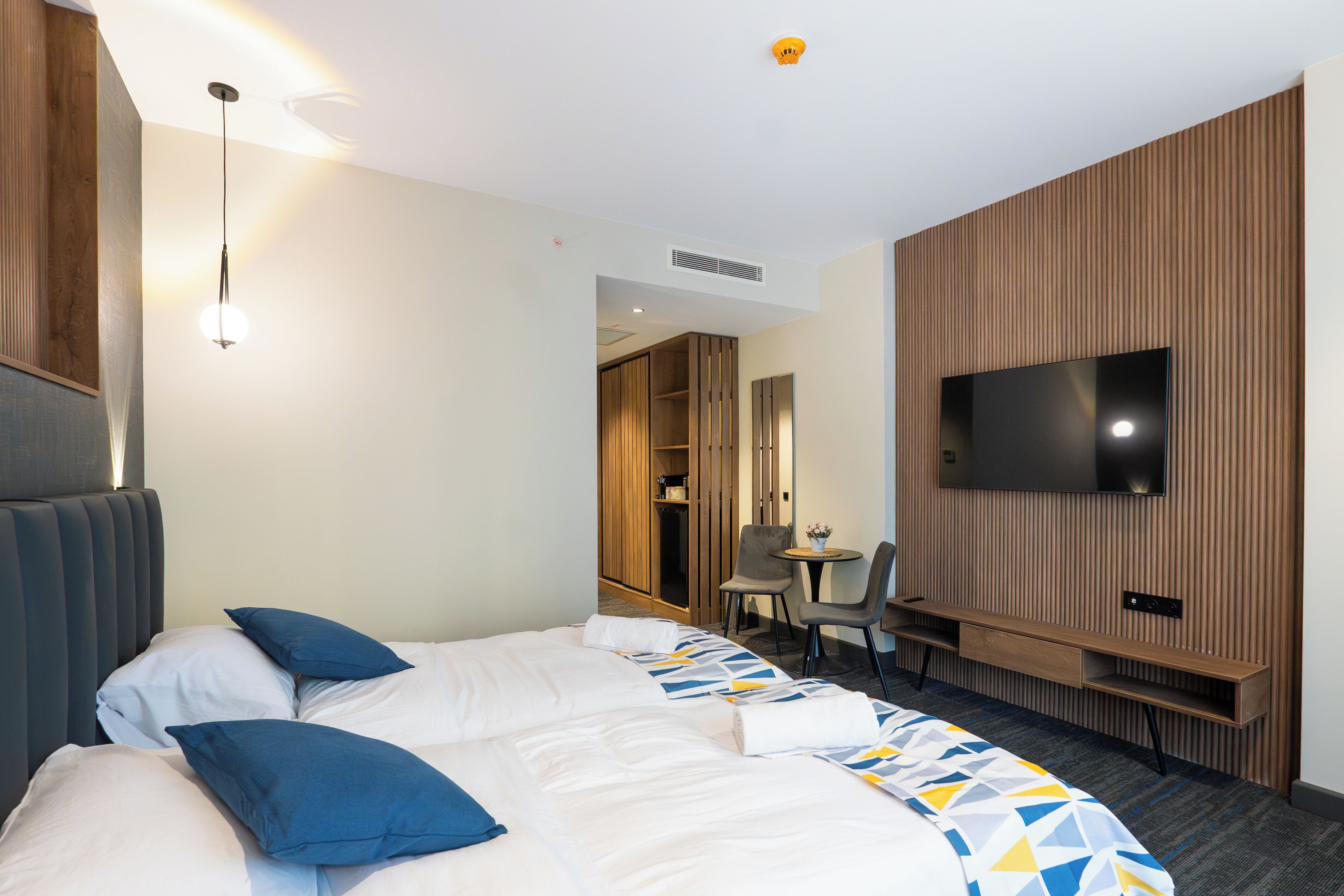 A hotel room with a large bed, a desk, a chair, a TV, and a wardrobe.
