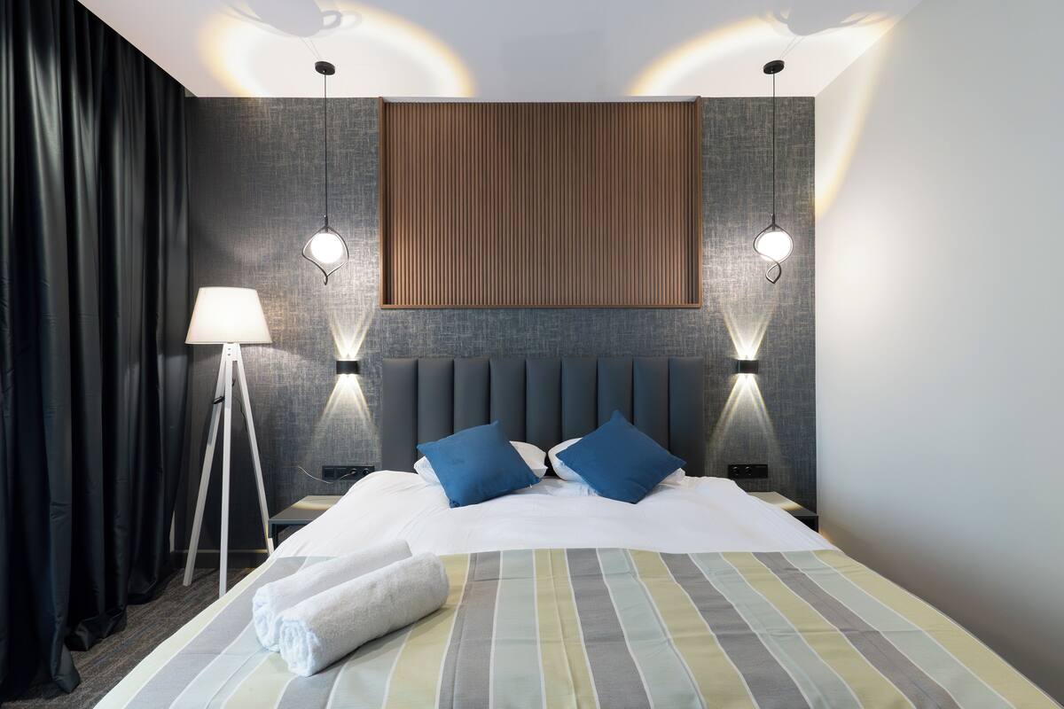 Une chambre d’hôtel moderne avec un grand lit, deux lampes de chevet, une lampe sur pied et une vue sur le panorama urbain.
