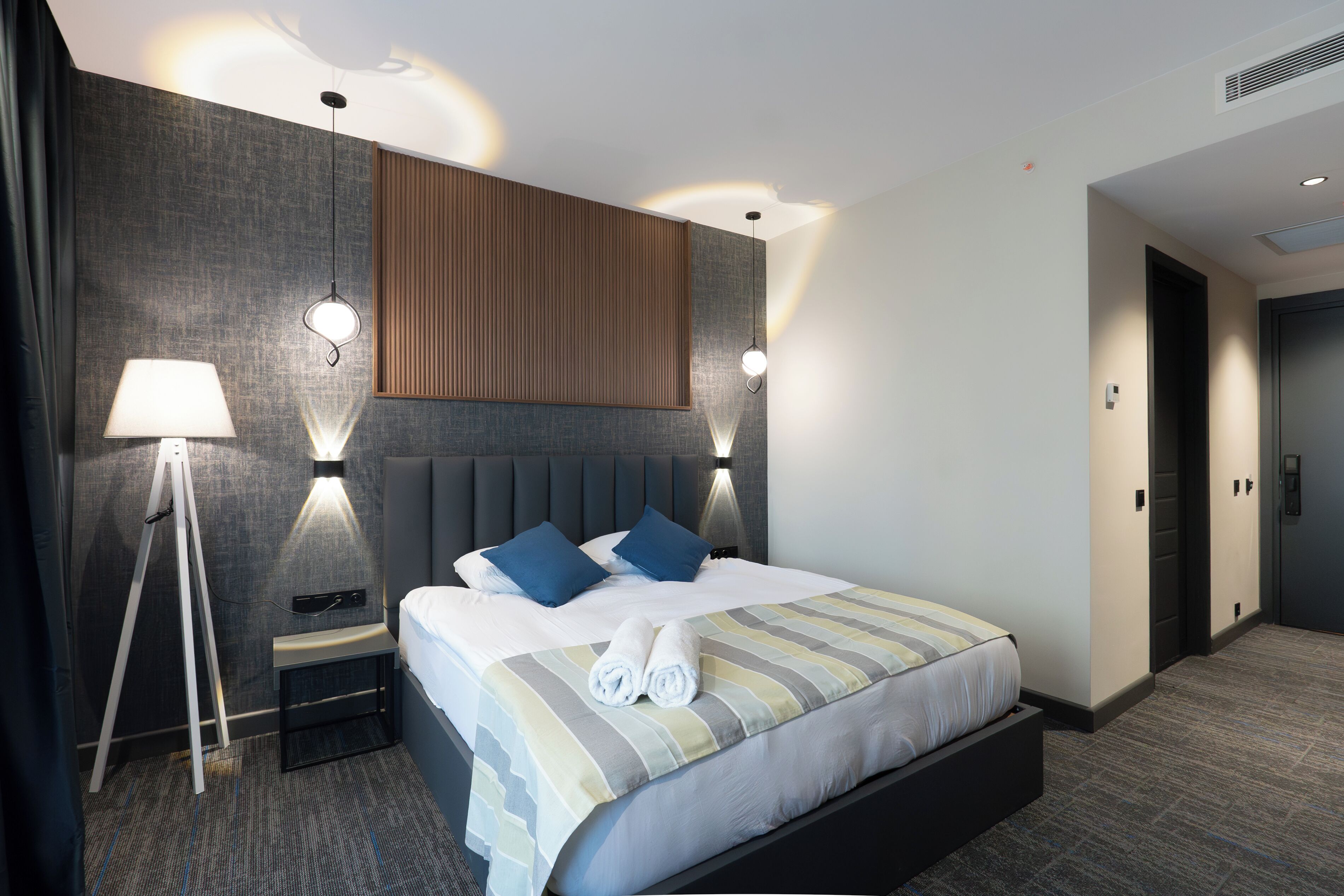 A modern hotel room with a large bed, bedside lamps, and a wooden panel wall.
