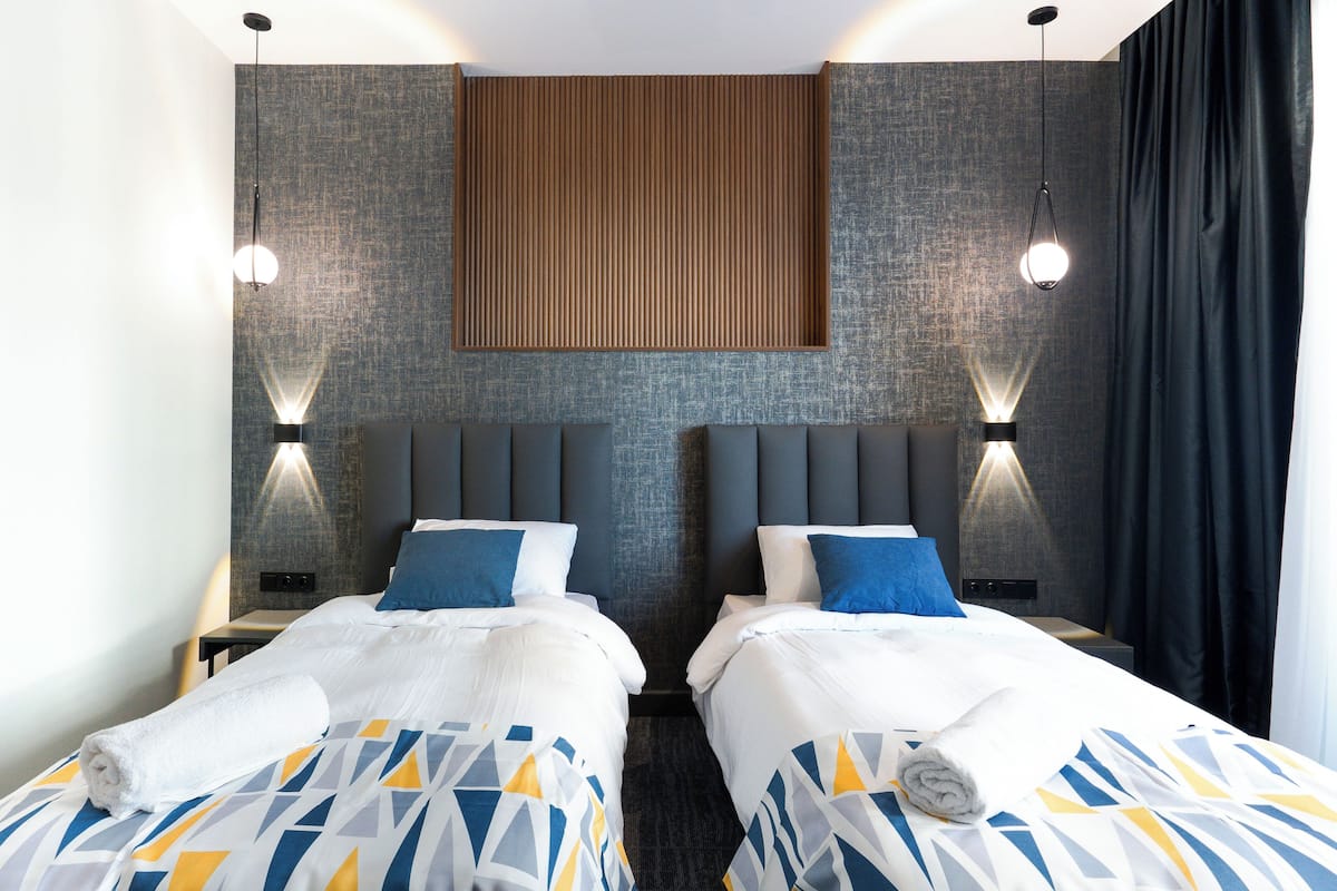 Une chambre d’hôtel avec deux lits, un mur recouvert de panneaux en bois et des lampes fixées au mur.