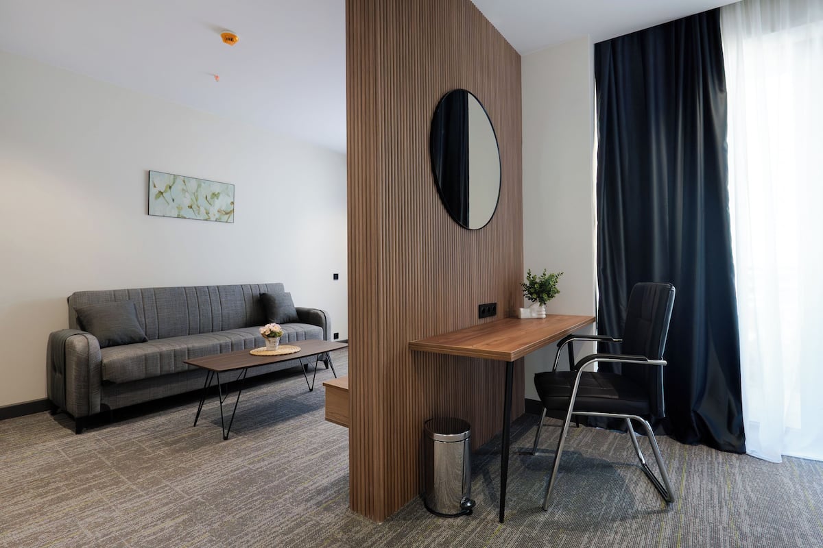 Une pièce moderne comprenant un canapé, un bureau en bois, une chaise, une poubelle et un grand miroir.