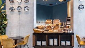 Un café con un mostrador central que exhibe pasteles y bebidas, rodeado de sillas amarillas.