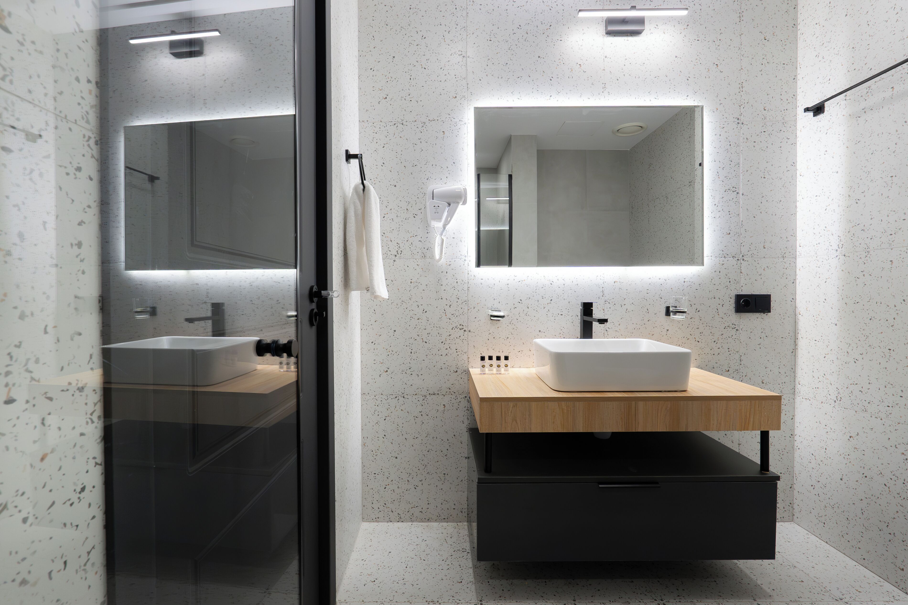 Une salle de bain moderne avec un grand miroir, deux lavabos, un porte-serviettes et un meuble encastré.