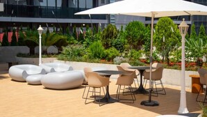 Un patio al aire libre con asientos modernos, una mesa y un gran paraguas.