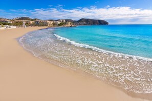 A beach with clear turquoise water, a sandy shore, and buildings in the background. - Rufete Apartment (Teulada)