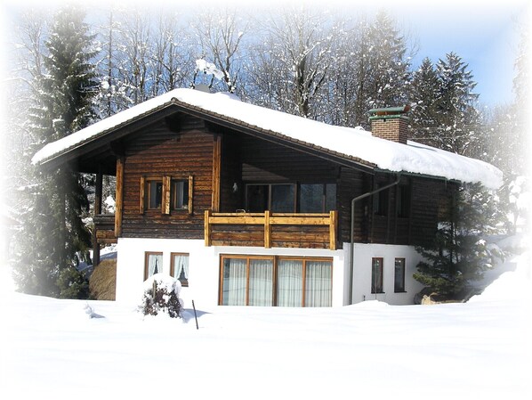 A log cabin with a balcony, surrounded by snow-covered trees.
