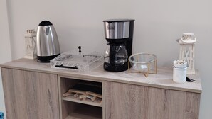 Una kitchenette con cafetera, hervidor y un mueble pequeño con estantes.