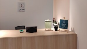 Un mostrador de recepción con un reloj, un cartel que indica la zona de recepción y un panel de información digital.