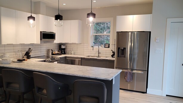 A modern kitchen with a central island, bar stools, stainless steel appliances, and pendant lighting. - Double D Ranch Guest House (Courtenay)