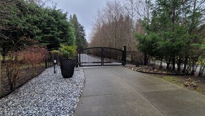 A gated driveway leading to a building with a gravel path and a large planter. - Double D Ranch Guest House (Courtenay)