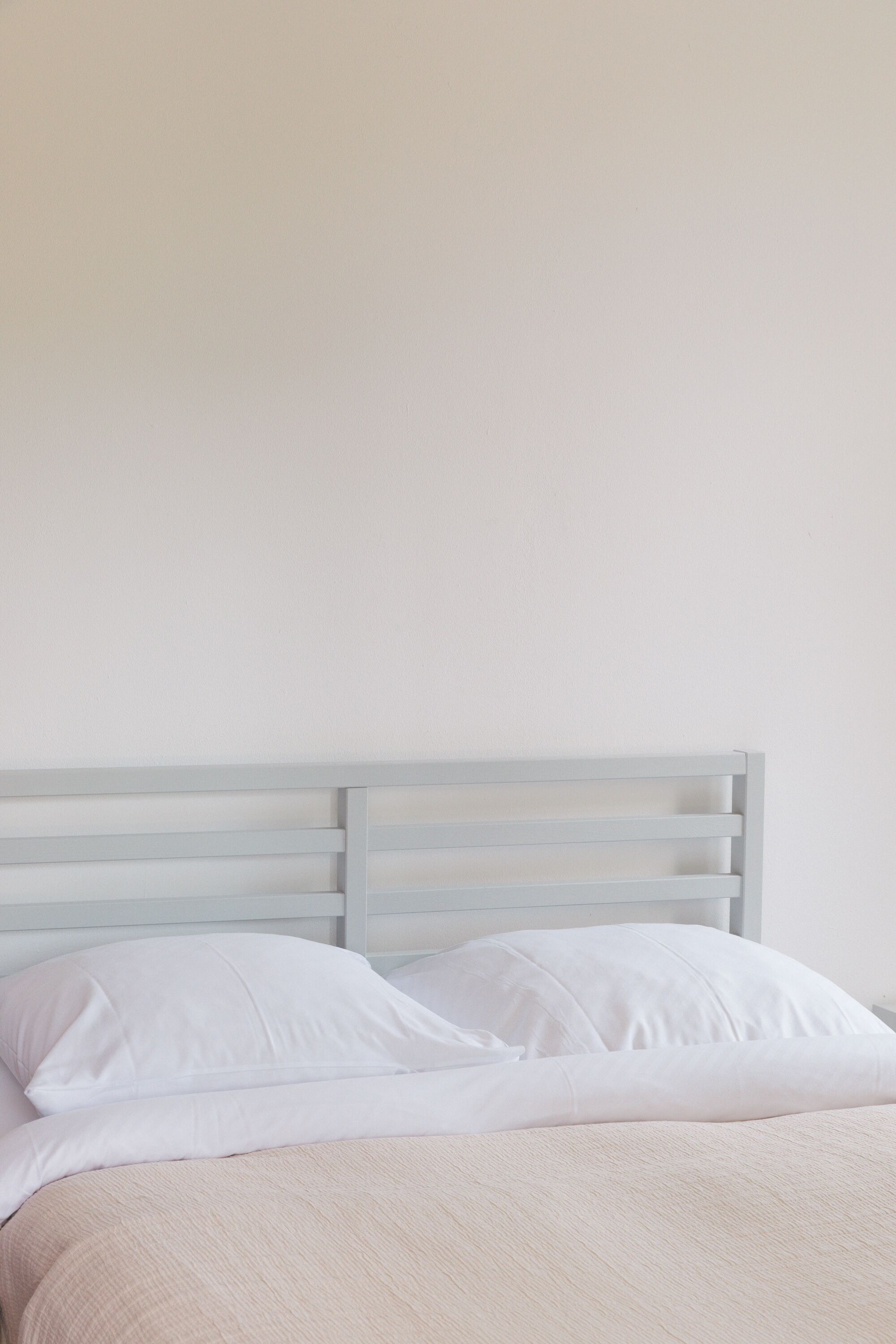 Een bed met wit beddengoed en een lichtkleurig hoofdbord.