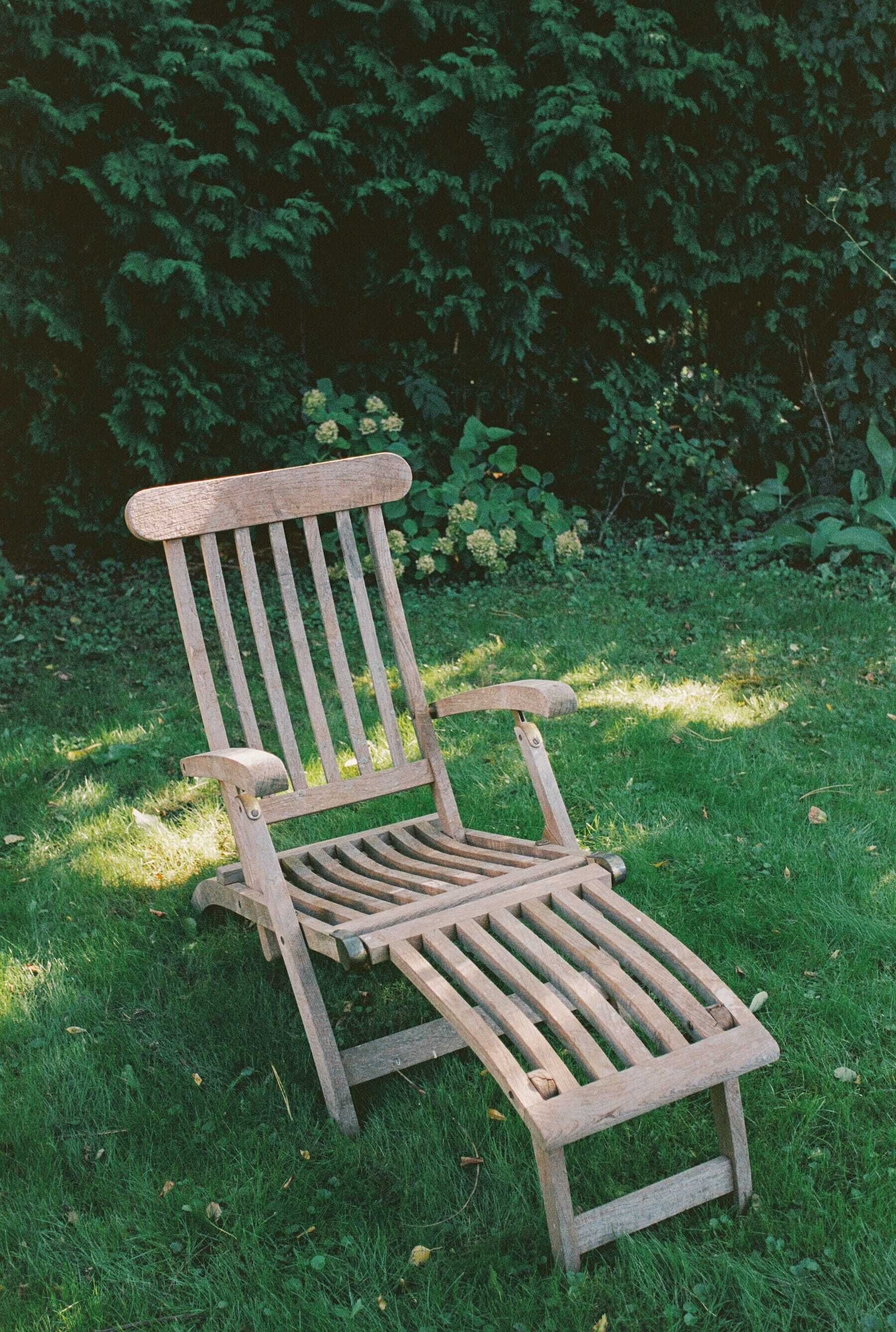 A wooden chair in a grassy area with dense foliage in the background.