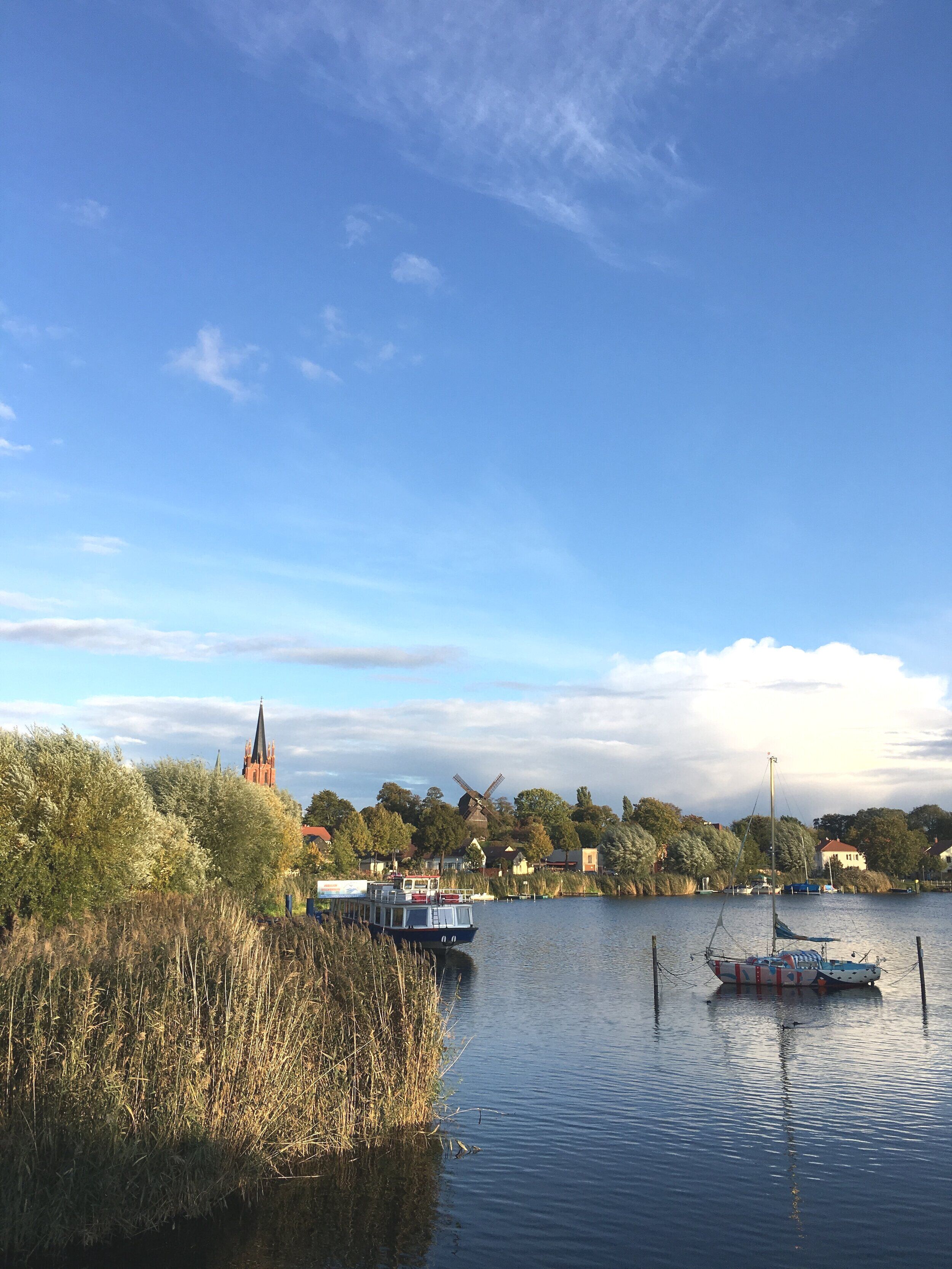 Ein ruhiger Fluss mit Booten, einer Windmühle und einer Kirche im Hintergrund.