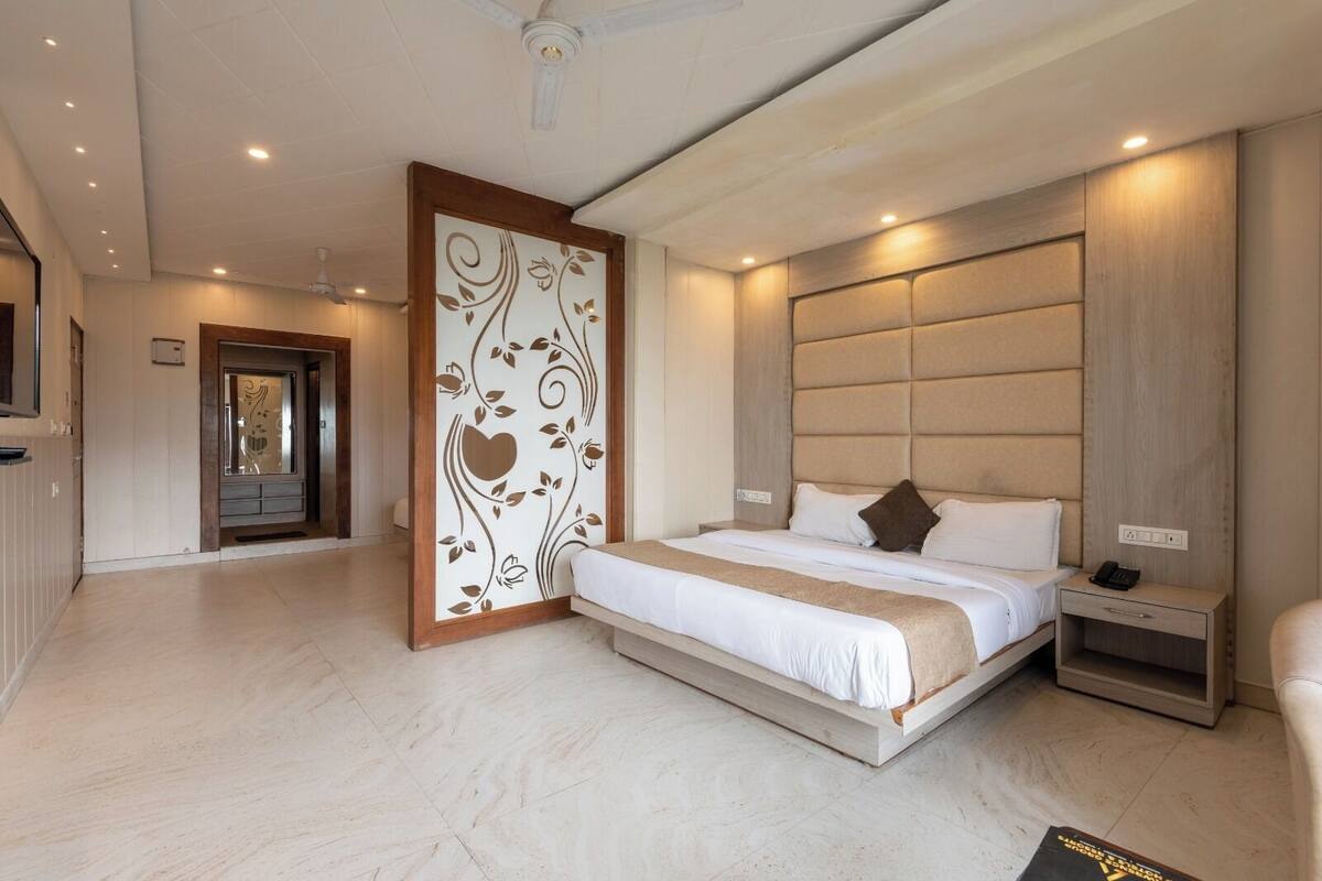 A modern hotel room with a large bed, a wooden headboard, a bedside table with a phone, and a decorative panel with floral designs.
