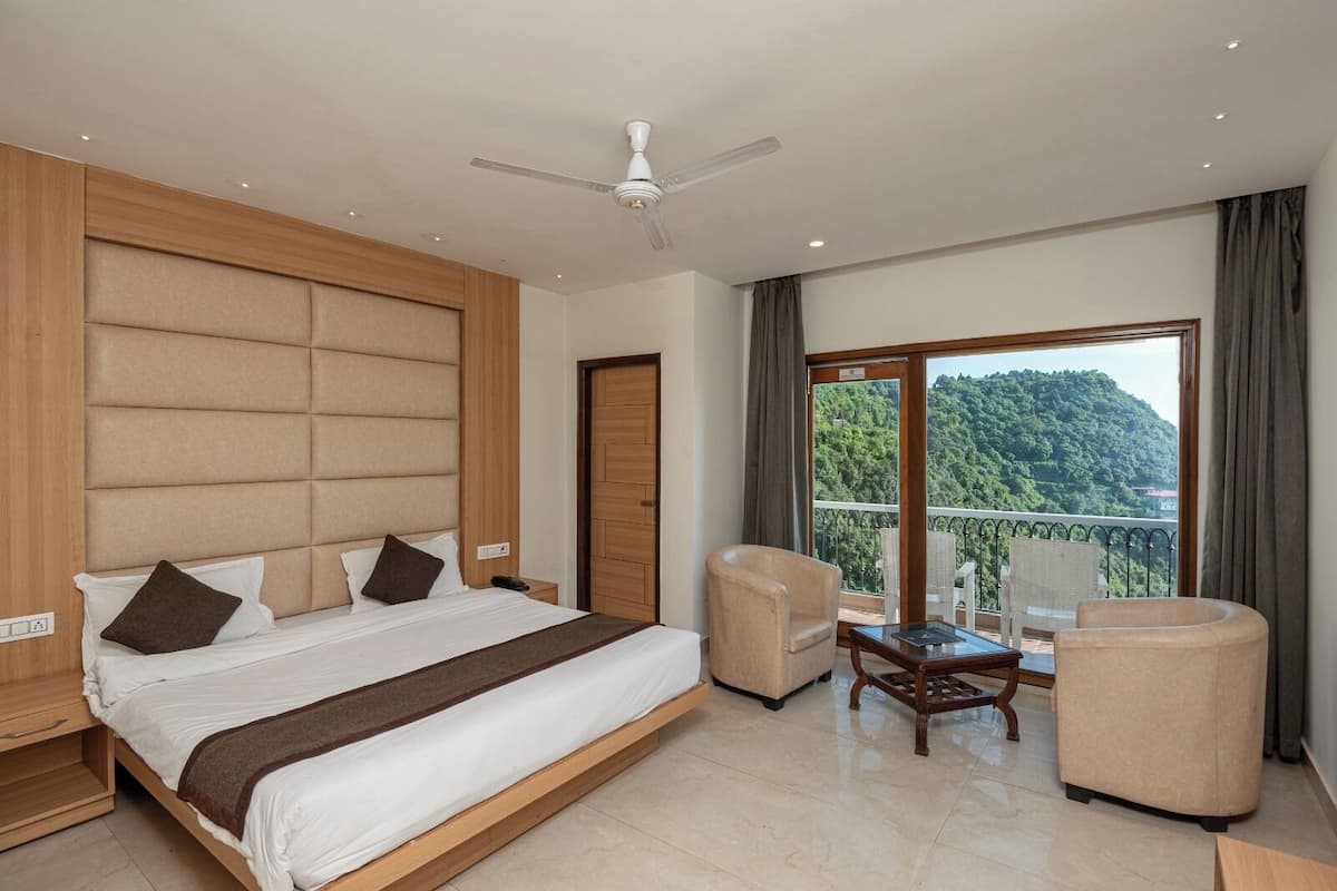 A modern hotel room with a large bed, a balcony with a view of the mountains, and a ceiling fan.