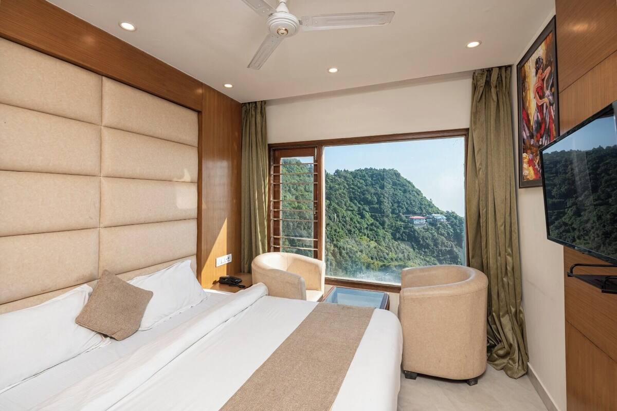 A hotel room with a large bed, a chair, a TV, and a view of a mountainous landscape.