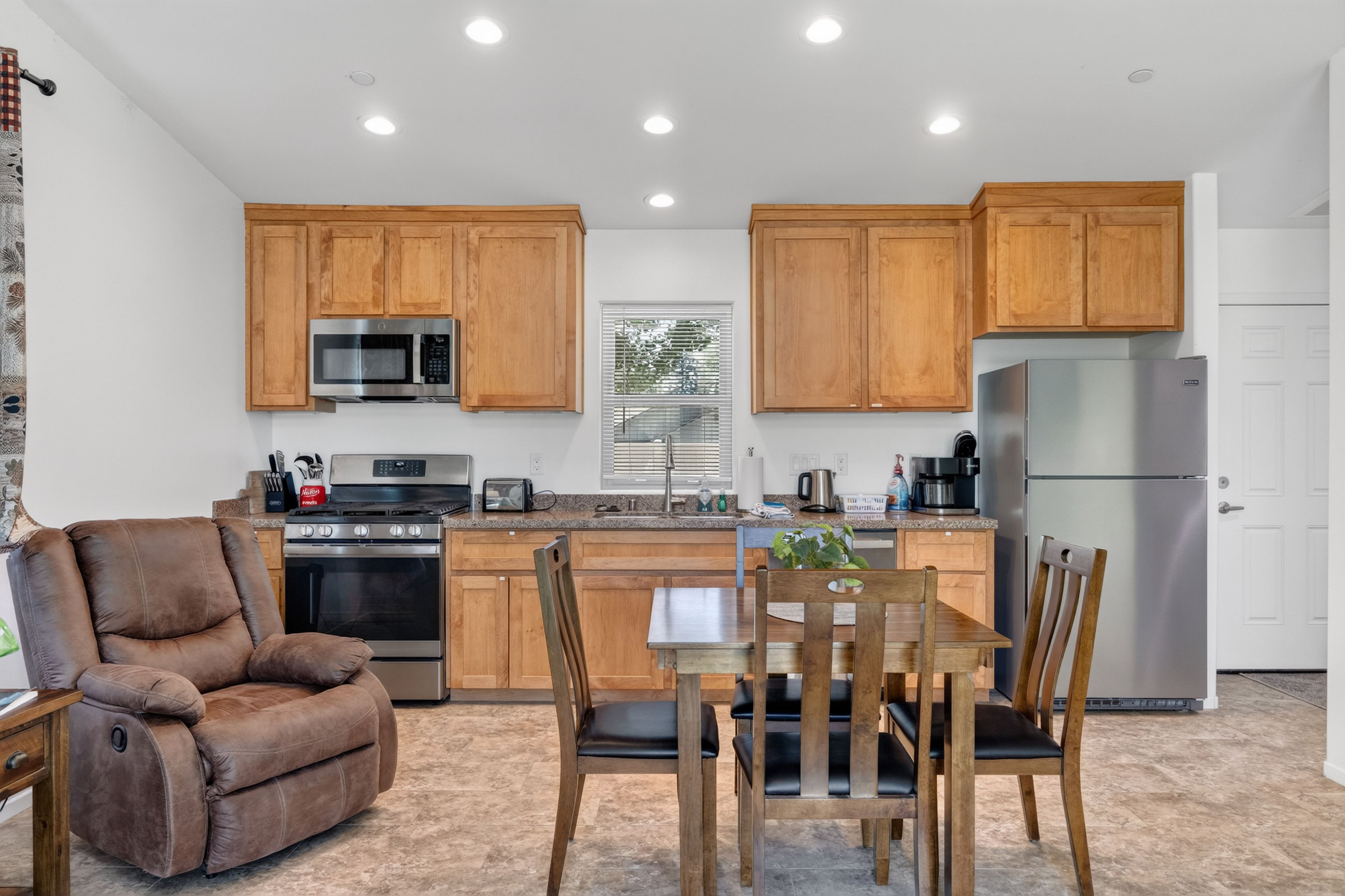 A modern kitchen with wooden cabinets, stainless steel appliances, and a dining area with a brown leather chair and wooden table.