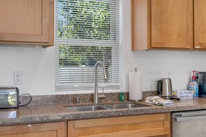 A kitchen with granite countertops, wooden cabinets, a stainless steel sink, and a window with blinds.