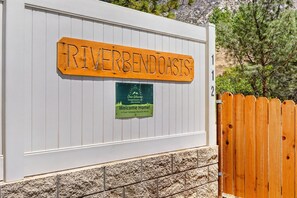A wooden sign with 'RIVERBENDOASIS' and a smaller sign below welcoming visitors to a vacation rental.