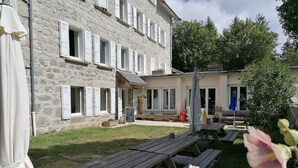 A stone building with white shutters, outdoor seating, and picnic tables. - Group gîte with single rooms, no dormitories, in the heart of nature. (Le Chambon-sur-Lignon)