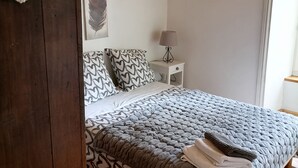 A bedroom with a wooden floor, a bed with patterned bedding, a bedside table with a lamp, and a hanging light fixture. - Group gîte with single rooms, no dormitories, in the heart of nature. (Le Chambon-sur-Lignon)