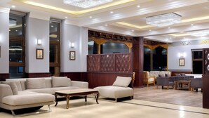 A spacious lobby with a sectional sofa, a wooden coffee table, and a seating area with armchairs and a small table. - Hotel Samaya (Leh)