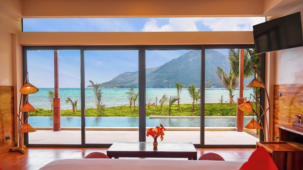 A hotel room with a large window offering a view of a pool and mountains. - Chaloklum Residences by Kupu Kupu Phangan (Ko Pha-ngan)