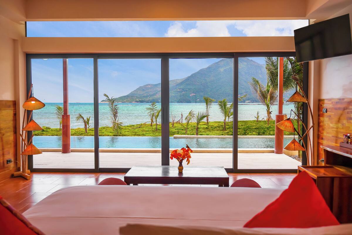 A hotel room with a large window offering a view of a pool and mountains.