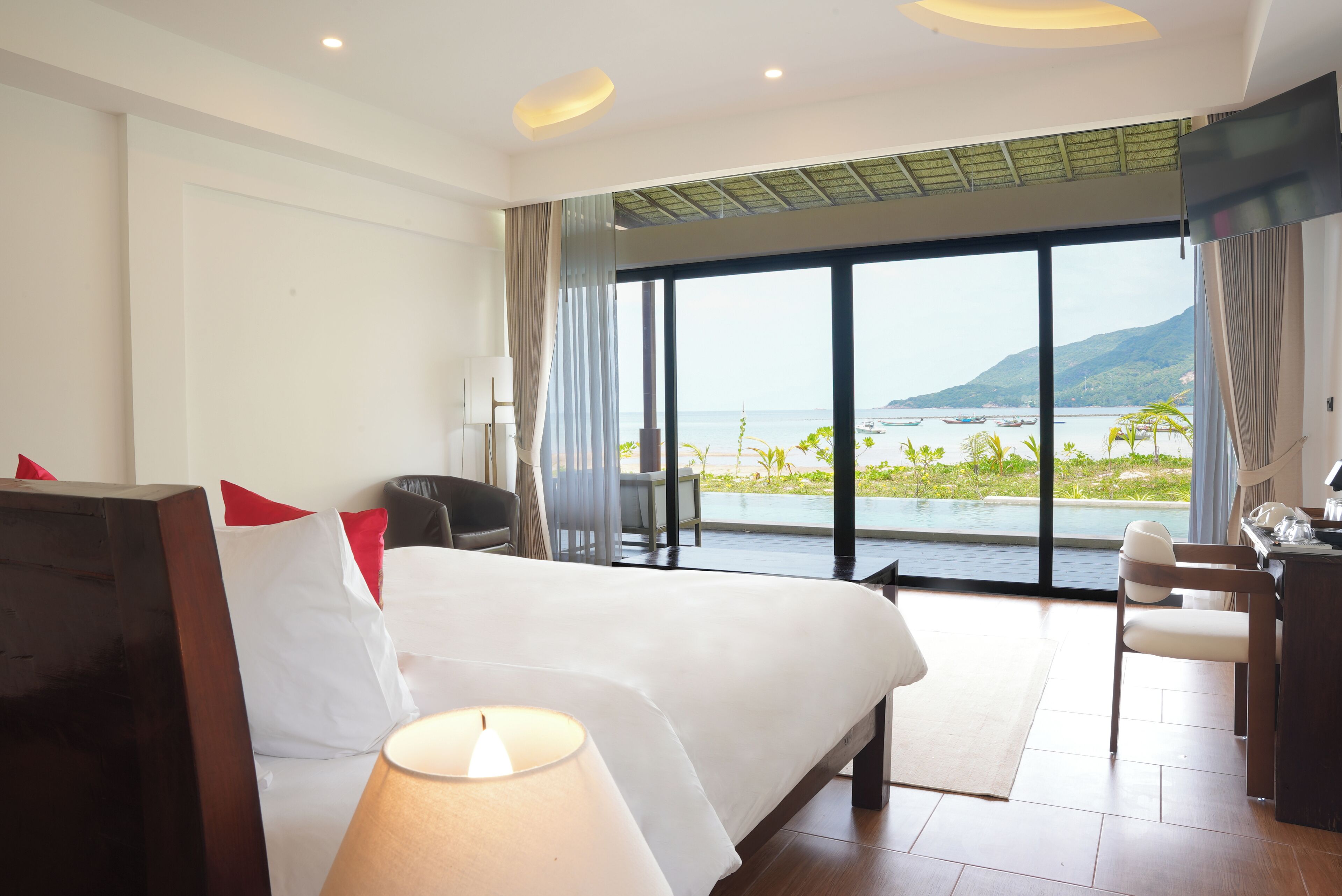 A hotel room with a large bed, a desk, and a view of the sea.