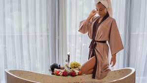 A person in a bathrobe sitting in a large bathtub with flowers and a bottle. - Chaloklum Residences by Kupu Kupu Phangan (Ko Pha-ngan)