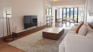 A modern living room with a flat-screen TV, a large wooden coffee table, and a white sofa. - Chaloklum Residences by Kupu Kupu Phangan (Ko Pha-ngan)