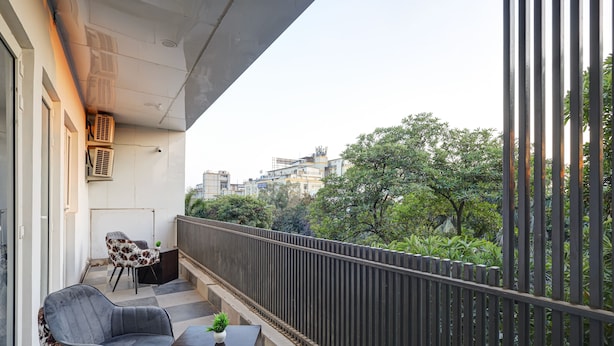 A balcony with a sofa, a small table, and a potted plant. - Hotel Warm Welcome Inn Noida Sector 26 (Noida)