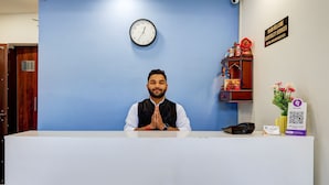 A hotel reception desk with a clock, a signboard, and a QR code for digital services. - Hotel Warm Welcome Inn Noida Sector 26 (Noida)