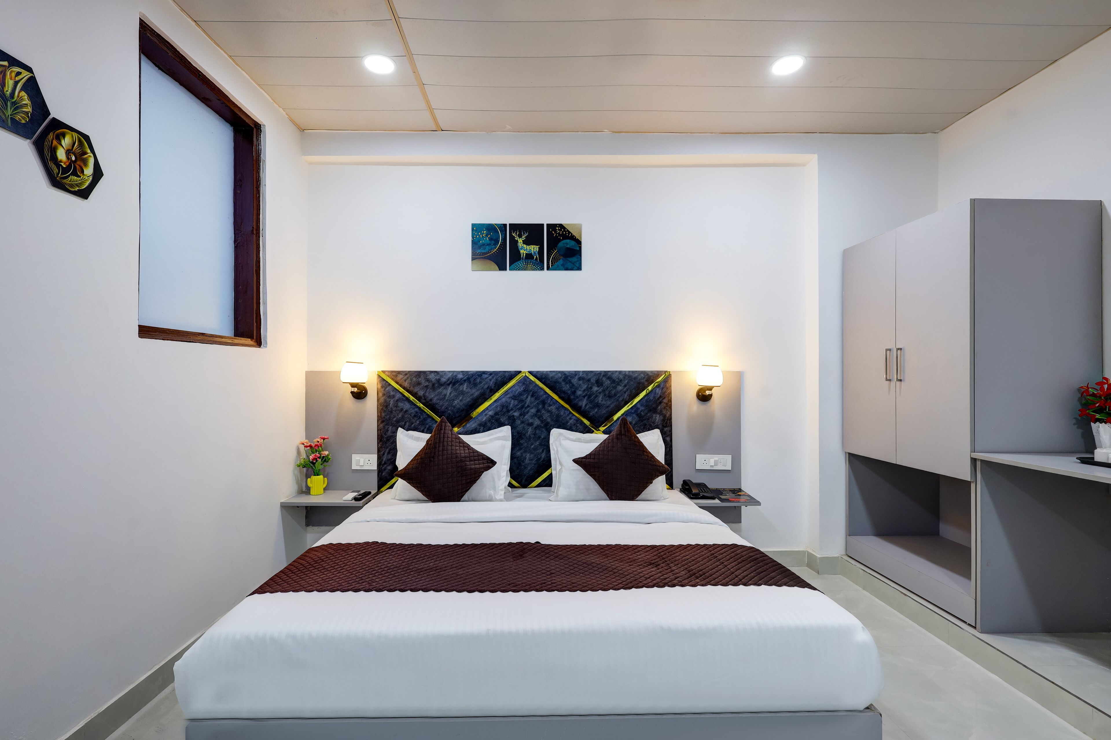 Una habitación de hotel moderna con una cama grande, mesitas de noche, un armario y obras de arte colgadas en la pared.