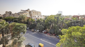 A multi-story building with a flat roof and a balcony, surrounded by dense greenery and parked vehicles. - Hotel Warm Welcome Inn Noida Sector 26 (Noida)