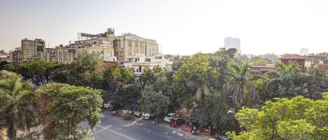 Un edificio de varios pisos con techo plano y balcón, rodeado de abundante vegetación y vehículos estacionados.