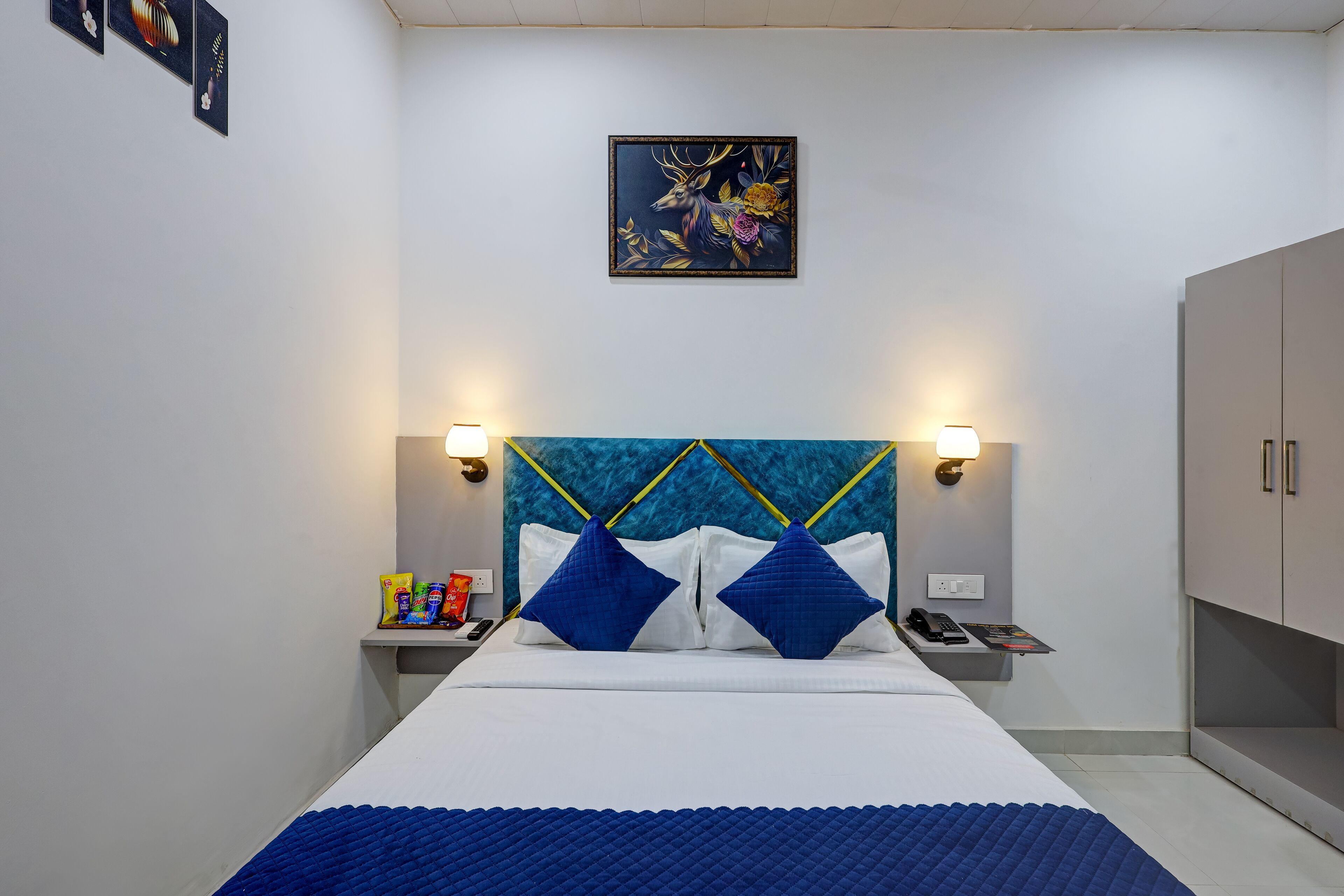 A neatly arranged hotel room with a bed, two bedside tables, a nightstand, a wall-mounted artwork, and a wardrobe.