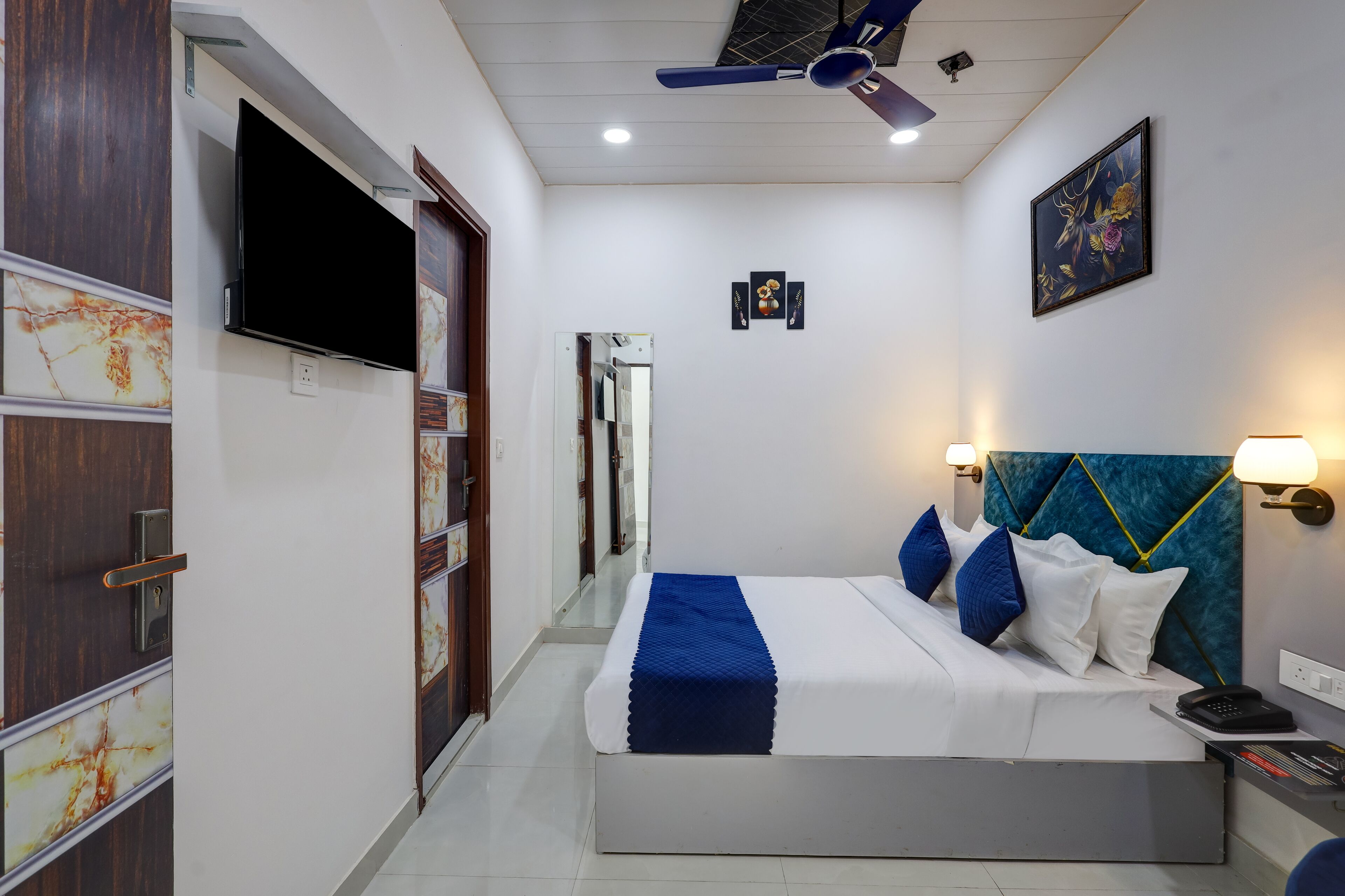 A hotel room with a bed, a TV, a ceiling fan, and a nightstand with a phone.