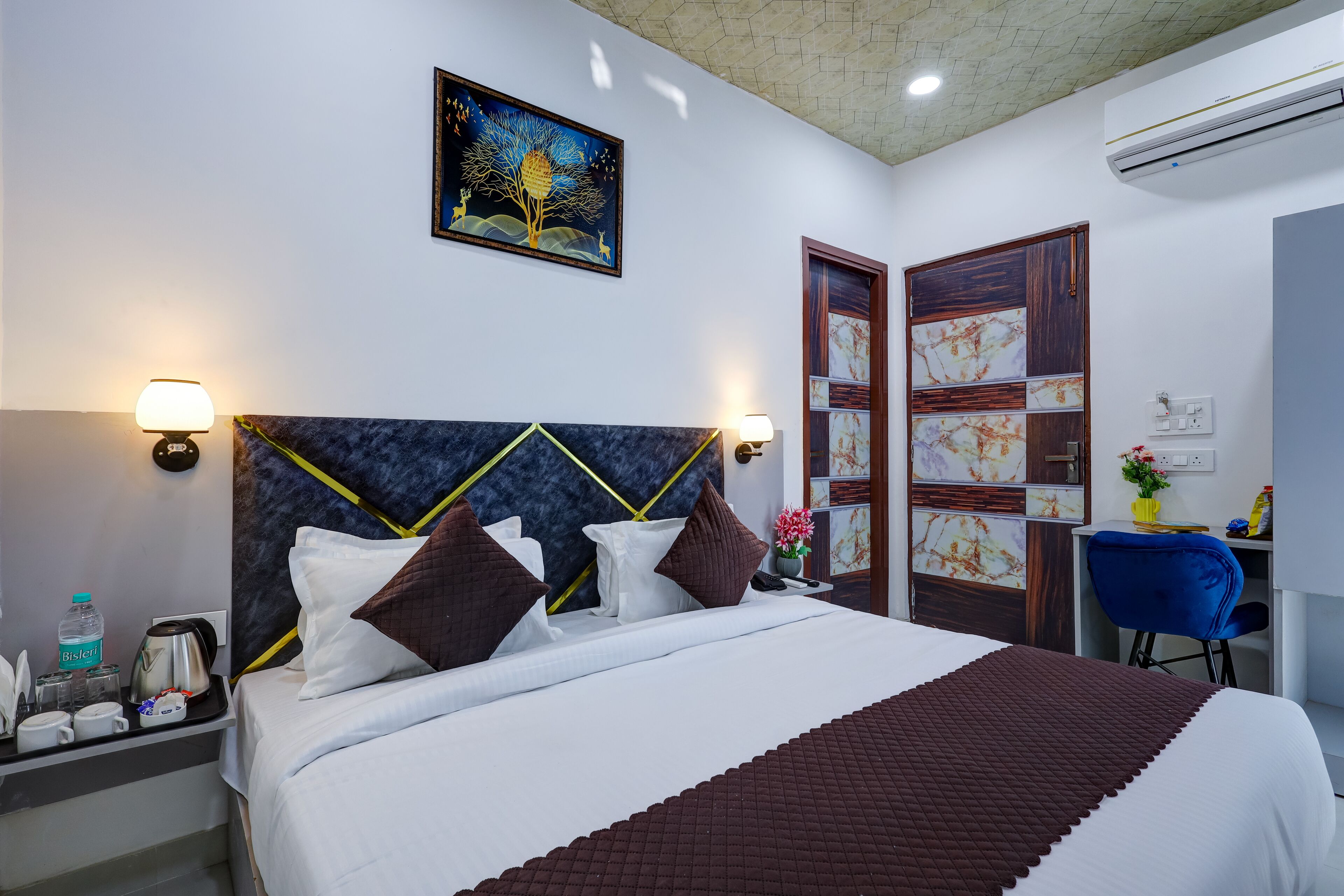 A hotel room with a large bed, bedside lamps, a desk with a chair, and a painting on the wall.