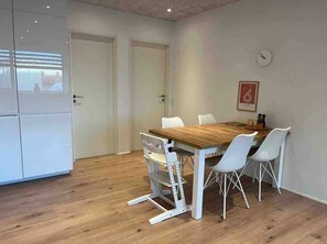 Un coin repas avec une table en bois et des chaises blanches, un réfrigérateur blanc et une horloge au mur.