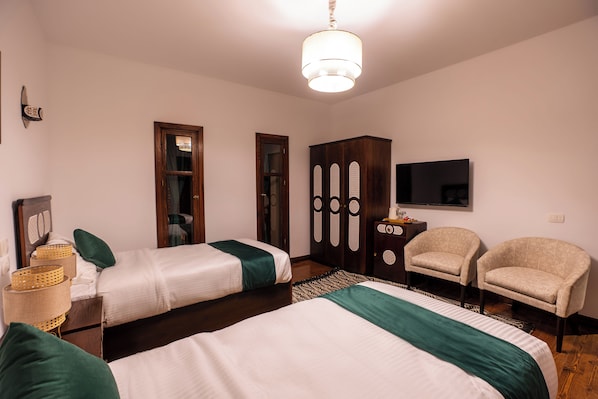 A bedroom with two beds, a wardrobe, a chair, and a television.