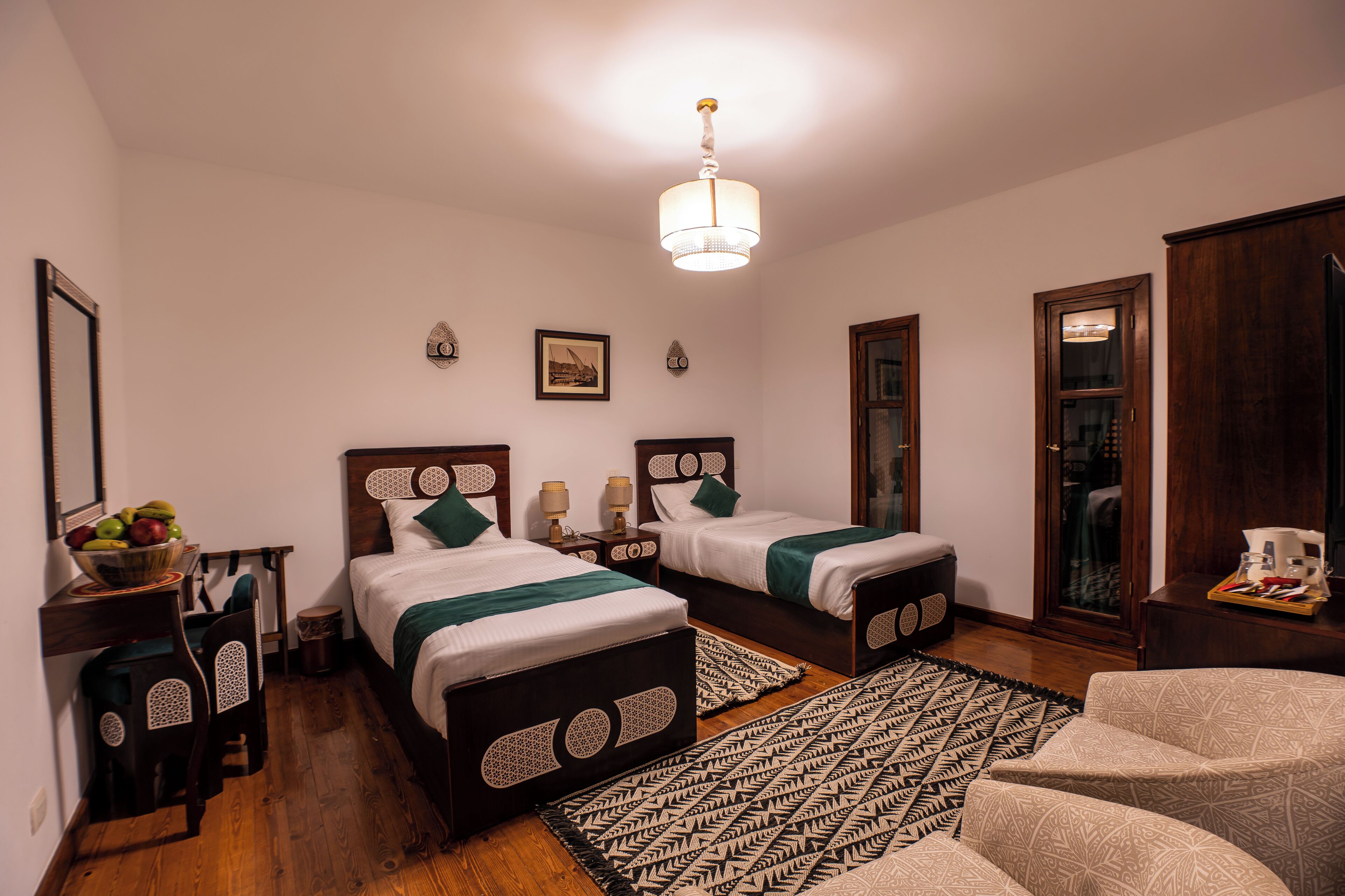 A room with two beds, a desk with a chair, a wooden floor, and a patterned rug.