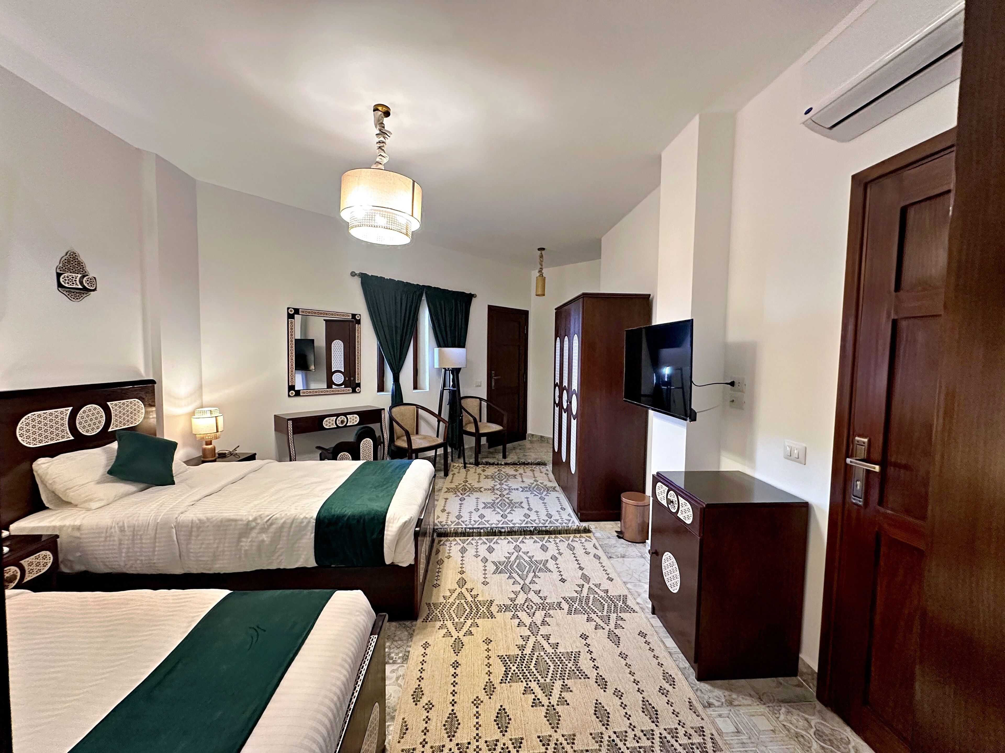 A hotel room with two beds, a desk, a chair, a TV, and a wardrobe.