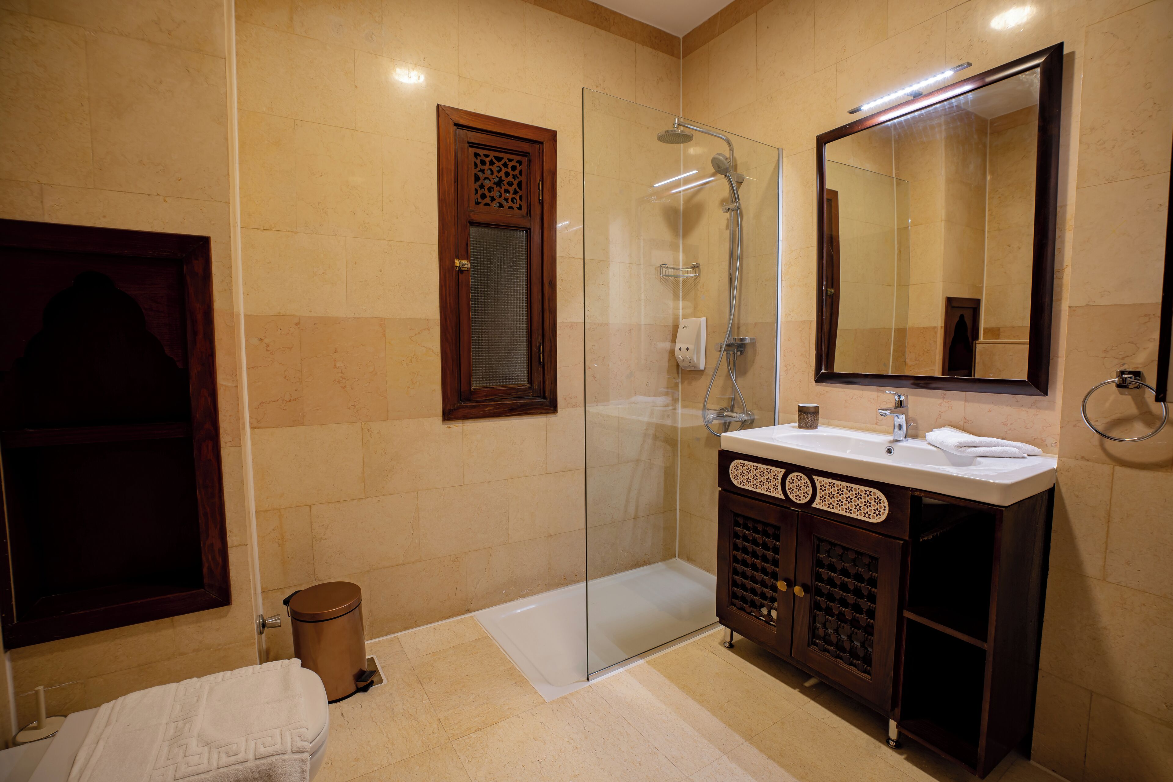 Un baño moderno con ducha envuelta en vidrio, un espejo grande y un tocador con lavamanos y toallero.