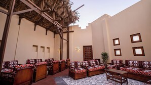A courtyard with wooden furniture, a patterned rug, and a thatched roof structure.